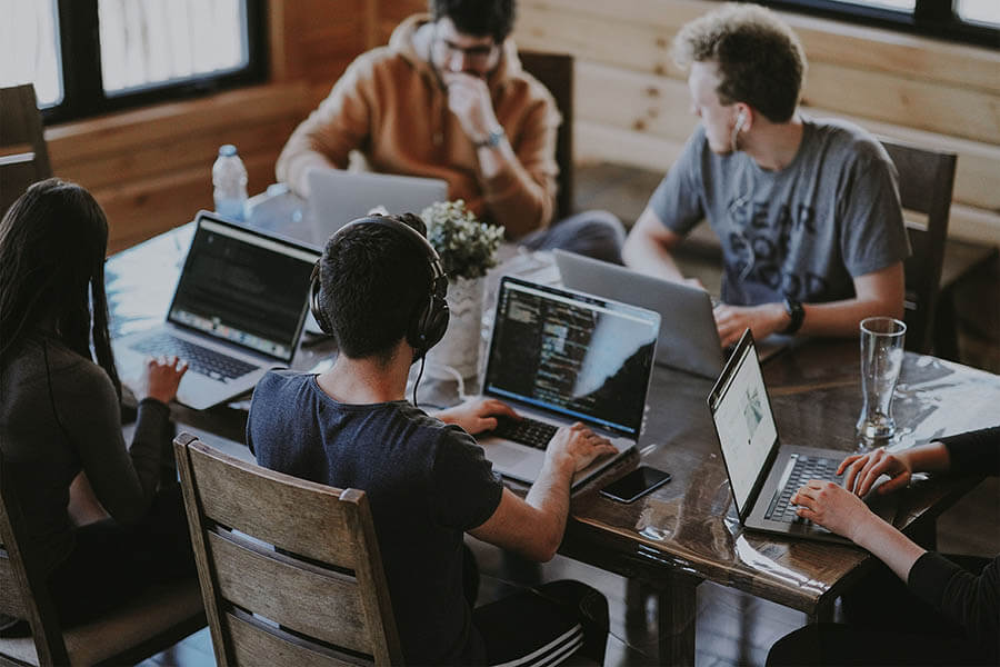 Cinco pessoas sentadas à mesa trabalhando em notebooks